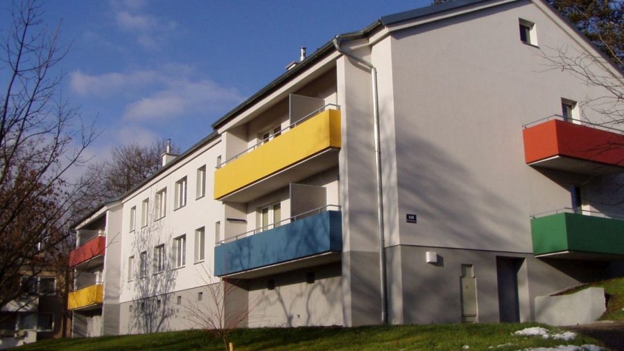 Mehrfamilienhaus mit bunten Balkonen unter blauem Himmel.