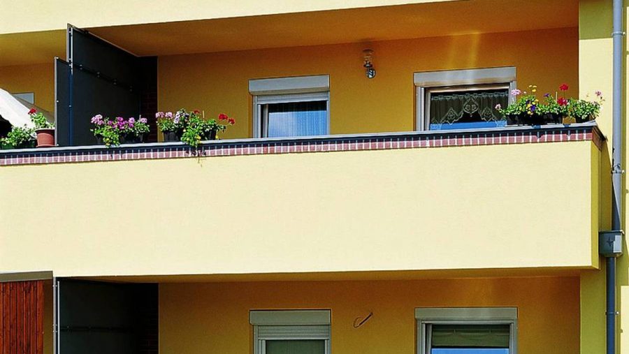 Gelber Balkon mit blühenden Pflanzen in Blumenkästen, moderne Gebäudefassade.