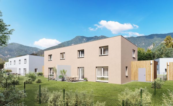 Moderne Wohnhäuser mit Garten, im Hintergrund malerische Berge unter blauem Himmel.