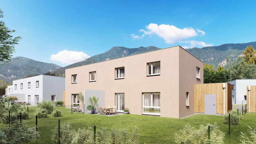 Moderne Wohnhäuser mit Garten, im Hintergrund malerische Berge unter blauem Himmel.