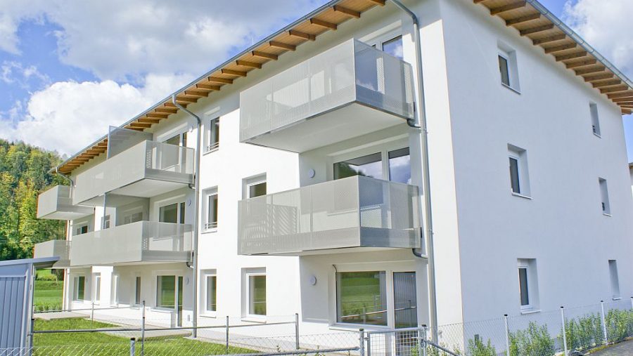 Modernes Mehrfamilienhaus mit Balkonen und Garten bei sonnigem Wetter.