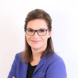 Eine professionelle Immobilienberaterin mit Brille und lächelndem Gesicht.