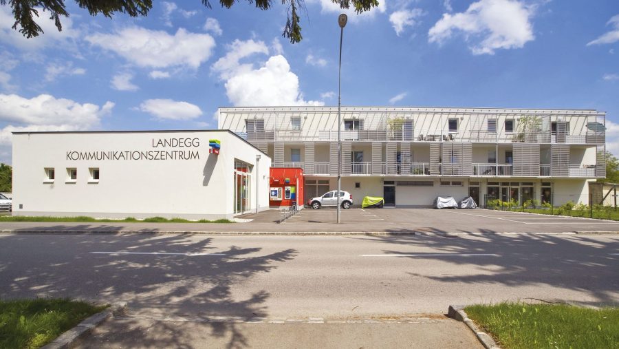 Moderne Gebäudeansicht mit Kommunikationseinrichtung und Fahrzeugen im sonnigen Außenbereich.