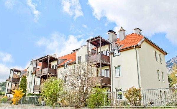 Mehrfamilienhaus mit roten Dächern, Balkonen und bewölktem Himmel im Hintergrund.