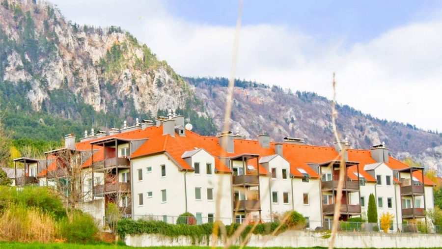 Wohngebäude vor Bergpanorama mit grüner Wiese und klarem Himmel.
