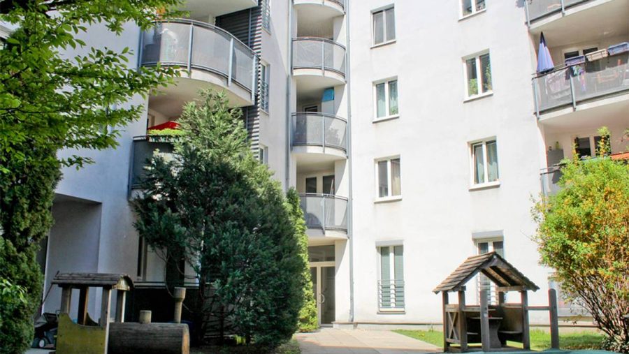 Mehrstöckiges Wohngebäude mit Balkonen und grünem Innenhof im Vordergrund.