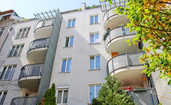 Wohnhaus mit modernen Balkonen und umliegender grüner Vegetation an einem sonnigen Tag.
