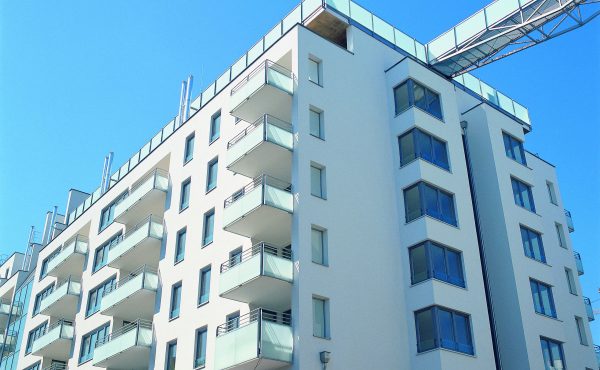 Mehrstöckiges Wohngebäude mit Balkonen und moderner Architektur unter blauem Himmel.