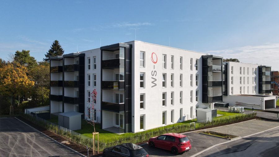 Moderne Wohnanlage mit geparkten Autos, blauem Himmel und umliegenden Bäumen.