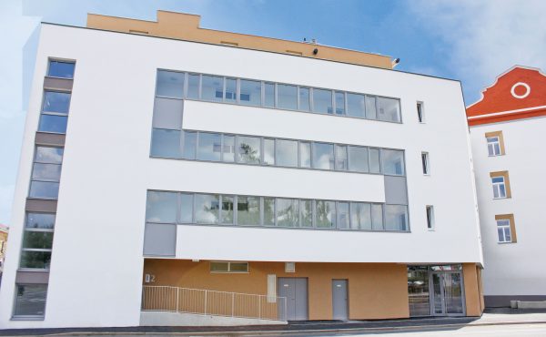 Modernes Geschäftsgebäude mit großen Fenstern und hellem Fassadenanstrich an einem sonnigen Tag.