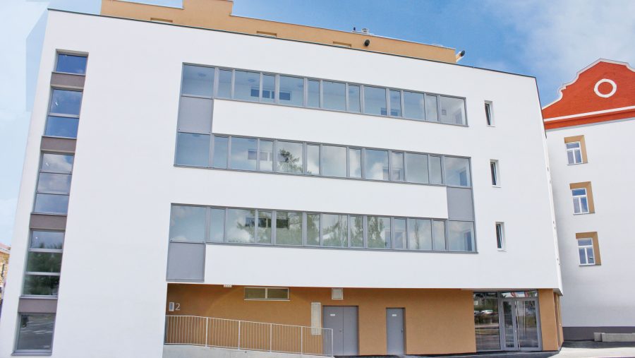 Modernes Geschäftsgebäude mit großen Fenstern und hellem Fassadenanstrich an einem sonnigen Tag.