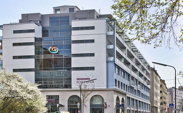 Modernes Bürogebäude mit Glasfassade in städtischer Umgebung, Frühling, blühende Bäume im Vordergrund.