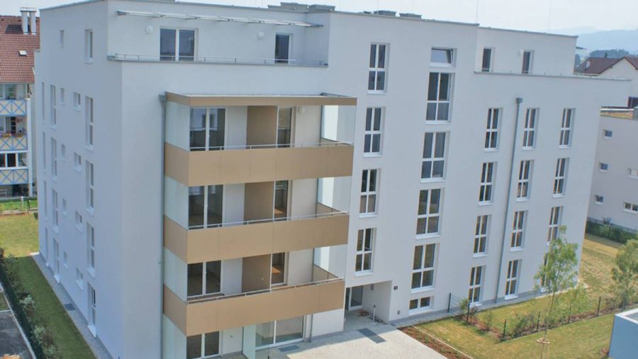 Modernes Mehrfamilienhaus mit Balkonen und großzügigen Fenstern, umgeben von Grasanlagen.