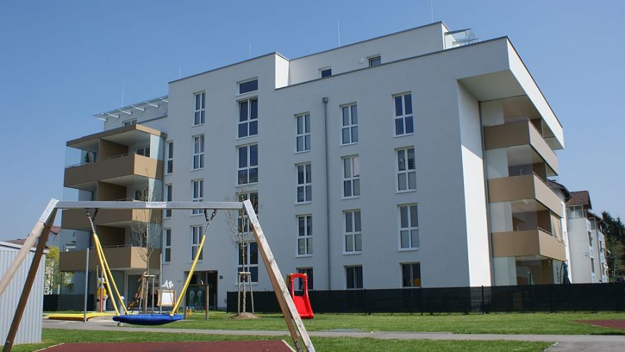 Moderne Wohnanlage mit Spielplatz vor blauem Himmel.