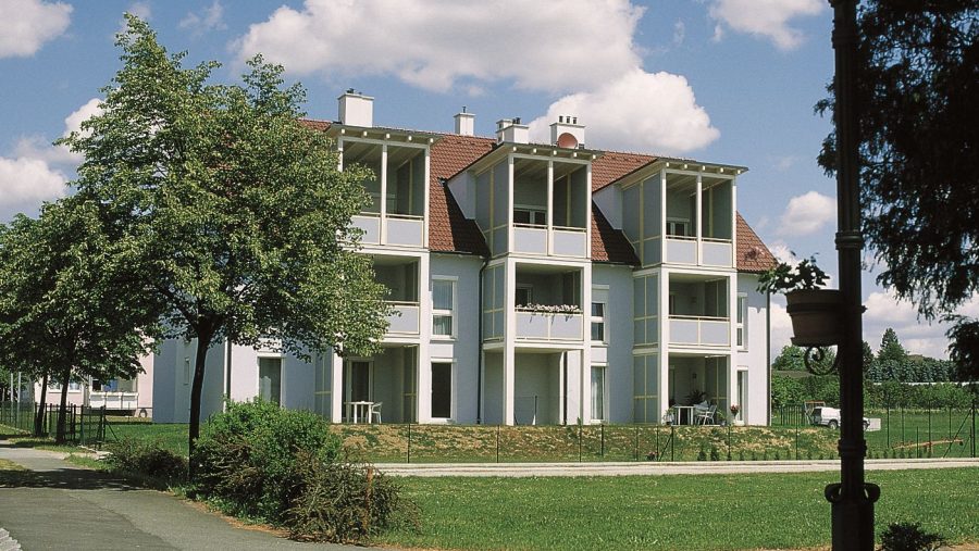Mehrfamilienhaus mit Balkonen und Bäumen bei Sonnenschein und blauem Himmel