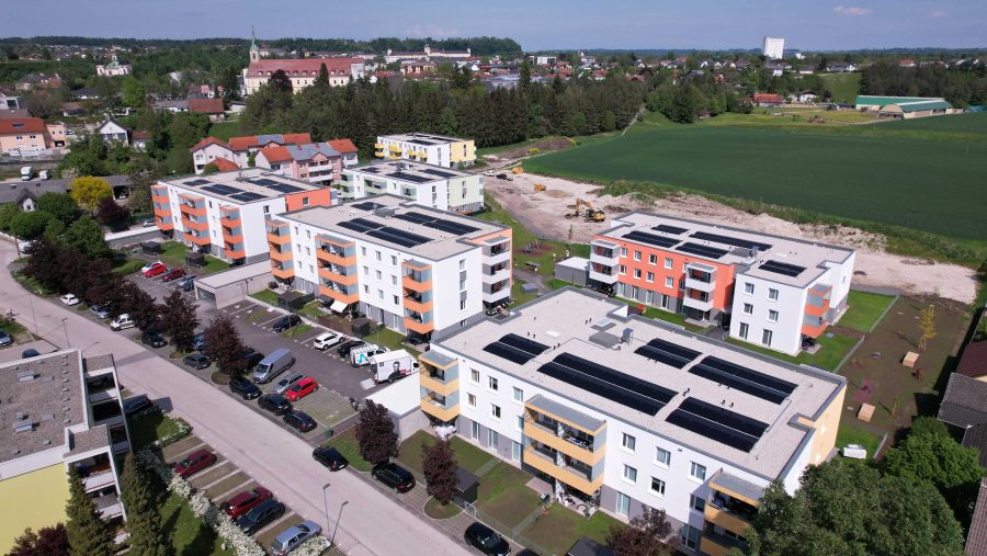 Luftaufnahme moderner Wohngebäude mit Solarmodulen und grüner Umgebung.