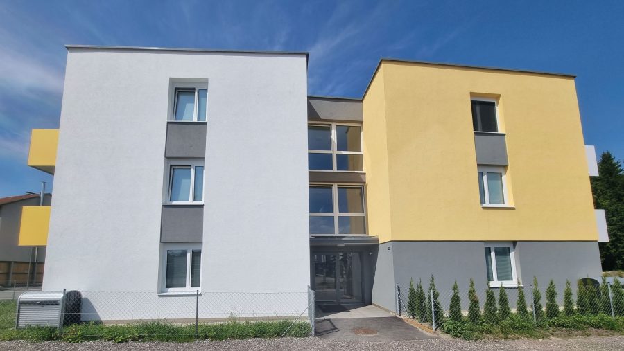 Modernes zweistöckiges Gebäude mit gelben und grauen Fassaden unter blauem Himmel.