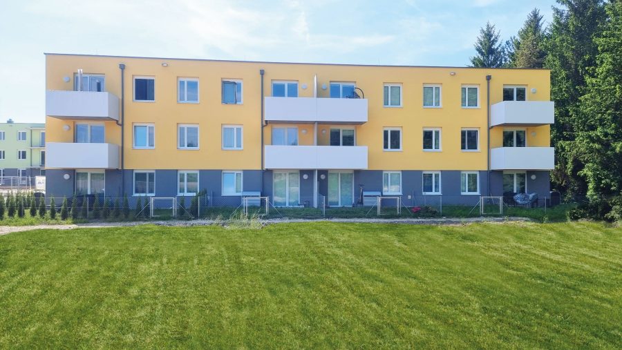 Gelbes Mehrfamilienhaus mit Balkonen vor einer grünen Rasenfläche.