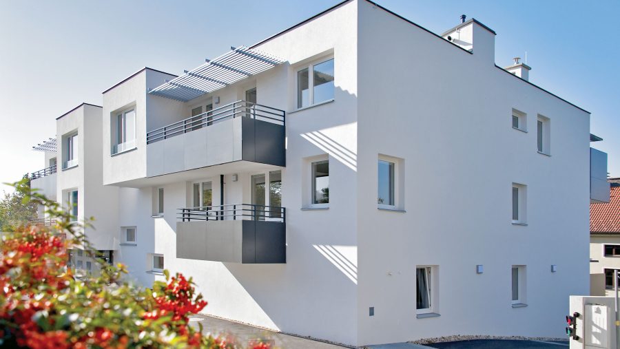 Moderne, weiße Wohngebäude mit Balkonen und blühenden Sträuchern im Vordergrund.