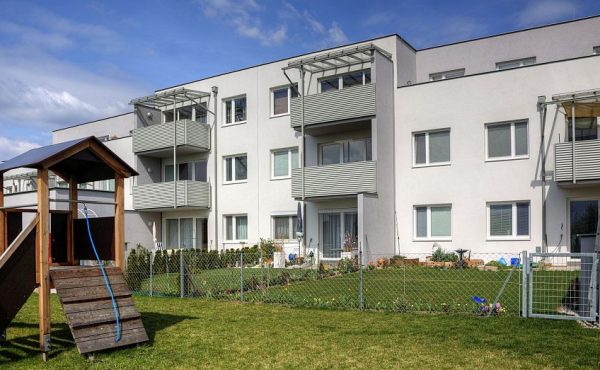 Wohnanlage mit Spielplatz im Vordergrund unter blauem Himmel.
