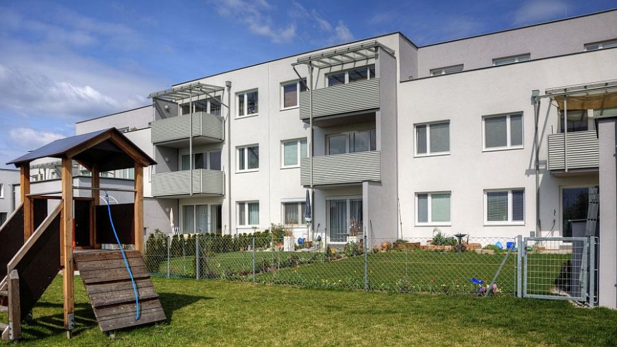 Wohnanlage mit Spielplatz im Vordergrund unter blauem Himmel.