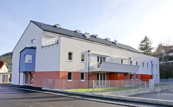 Modernes zweistöckiges Wohngebäude mit weißer Fassade und Balkonen an einem sonnigen Tag.