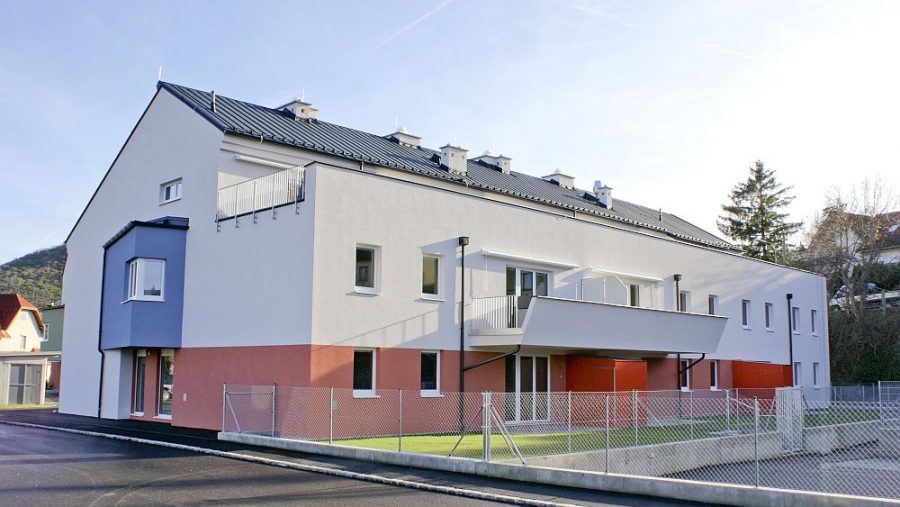 Modernes zweistöckiges Wohngebäude mit weißer Fassade und Balkonen an einem sonnigen Tag.