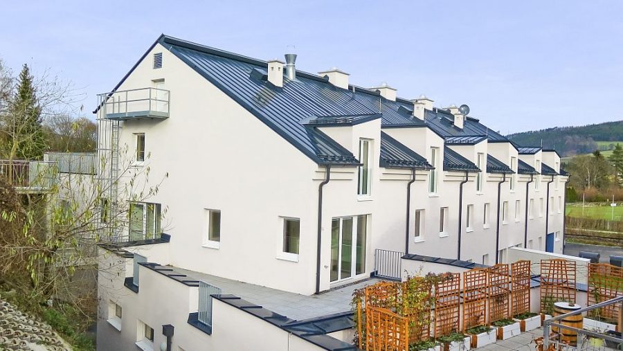 Mehrfamilienhaus mit modernen, weiß verputzten Wänden und Schrägdach in ländlicher Umgebung.