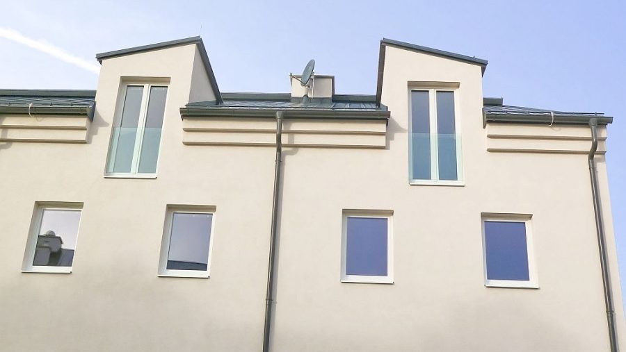 Mehrstöckiges modernes Wohnhaus mit weißer Fassade und blauen Akzenten, aufgenommen an einem sonnigen Tag.