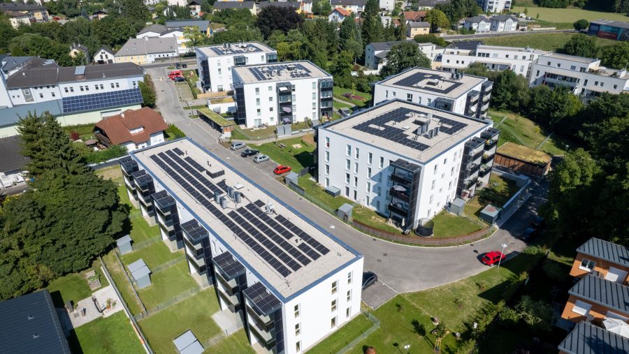 Luftaufnahme von Wohngebäuden mit Solarpanelen auf den Dächern in einem grünen Wohngebiet.