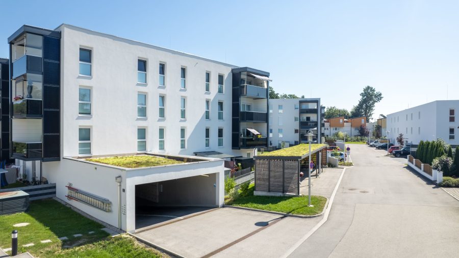 Moderne Wohnanlagen mit Parkplätzen und Grünflächen an einem sonnigen Tag.