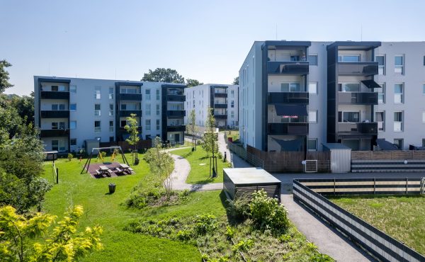Moderne Wohnanlage mit Spielplatz und Gartenfläche bei sonnigem Wetter.