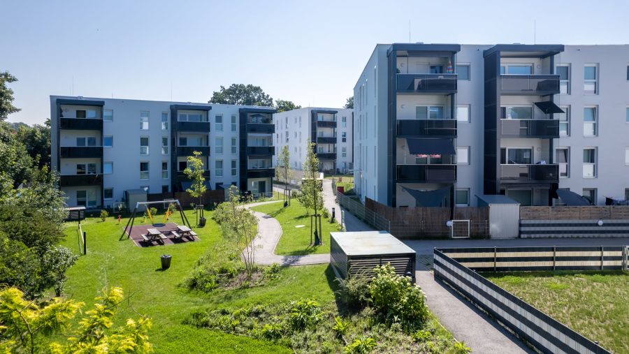 Moderne Wohnanlage mit Spielplatz und Gartenfläche bei sonnigem Wetter.