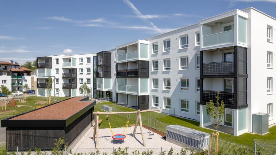 Mehrfamilienhaus mit Spielplatz im modernen Wohnkomplex bei blauem Himmel.