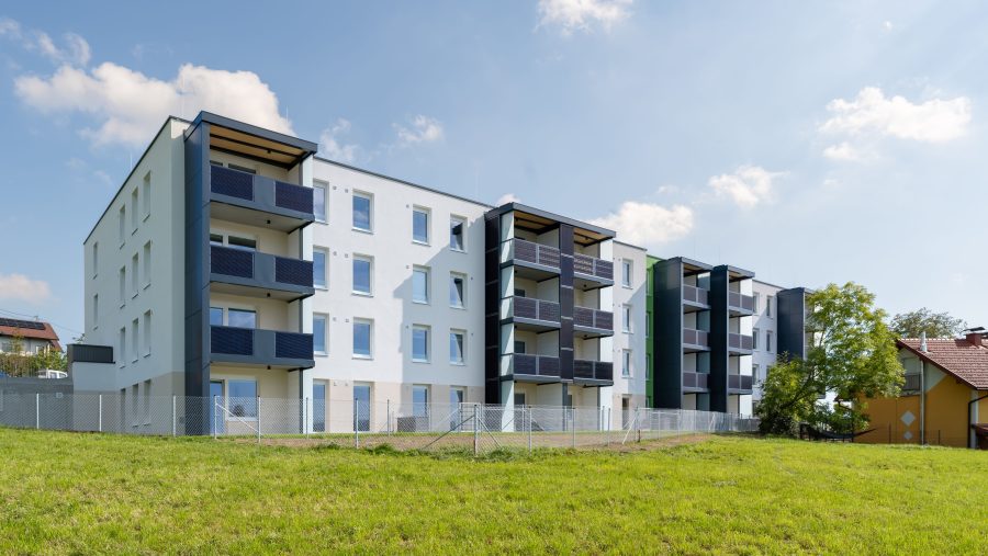 Mehrstöckiges Wohngebäude mit Balkon und Grünfläche im Vordergrund bei sonnigem Himmel.
