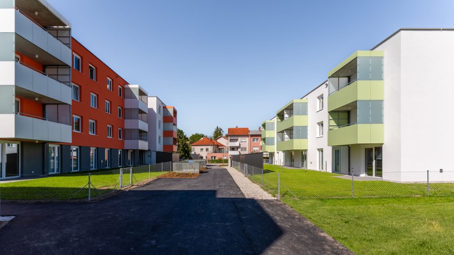 Moderne Wohngebäude mit bunten Fassaden und gepflegtem Grünflächen bei klarem Himmel.