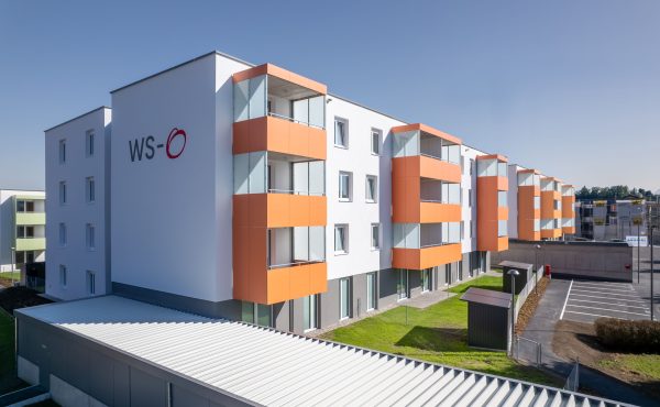 Moderne Wohnanlage mit orangenen Balkonen und klarer Architektur bei Sonnenschein.