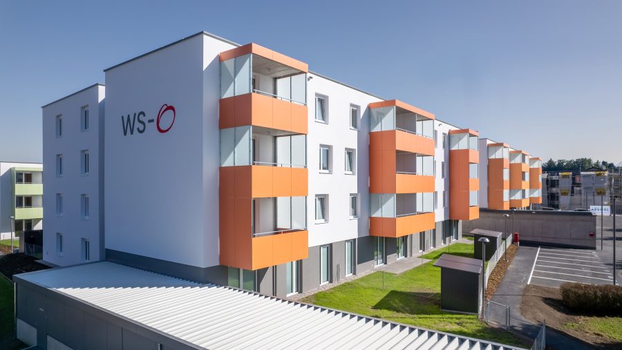 Moderne Wohnanlage mit orangenen Balkonen und klarer Architektur bei Sonnenschein.