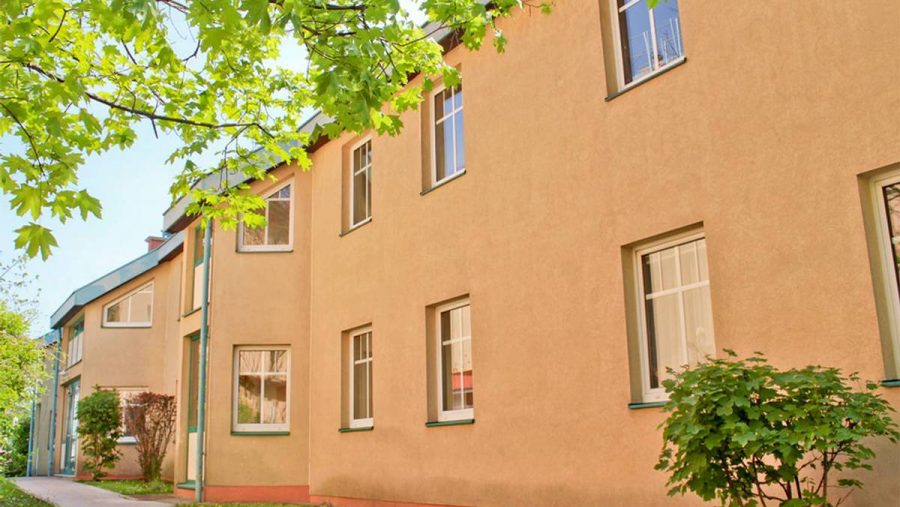 Wohngebäude mit Bäumen im Vordergrund an einem sonnigen Tag