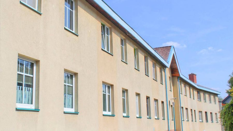 Langes Gebäude mit beigen Wänden und mehreren Fenstern unter blauem Himmel.