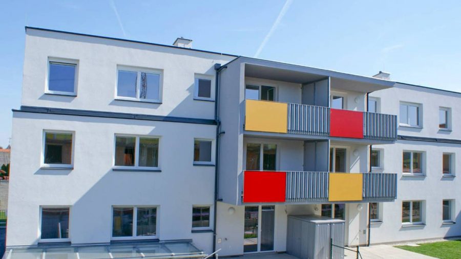 Modernes Wohngebäude mit farbigen Balkonen und blauer Fassade im Sonnenschein.