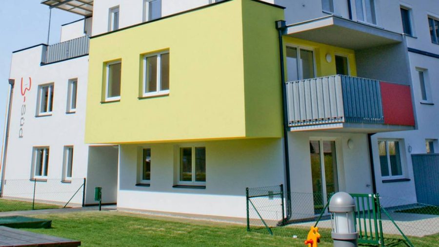 Modernes Wohngebäude mit buntem Balkon und Gartenbereich im Vordergrund.