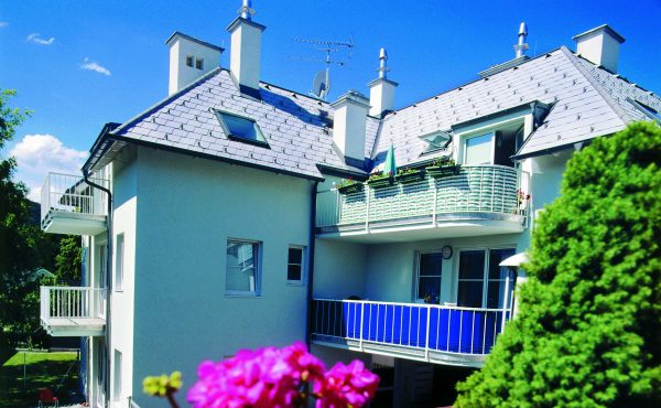 Modernes Wohngebäude mit Balkonen und Blumen vor blauem Himmel.