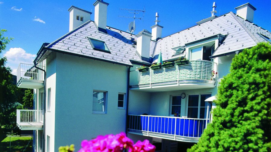 Modernes Wohngebäude mit Balkonen und Blumen vor blauem Himmel.