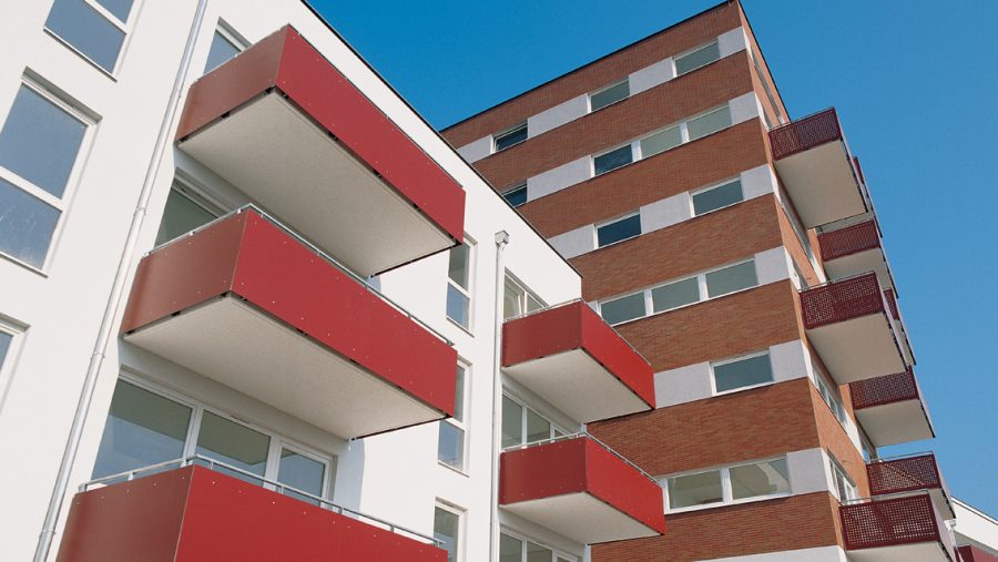 Moderne Wohngebäude mit roten Balkonen und blauer Himmel im Hintergrund.