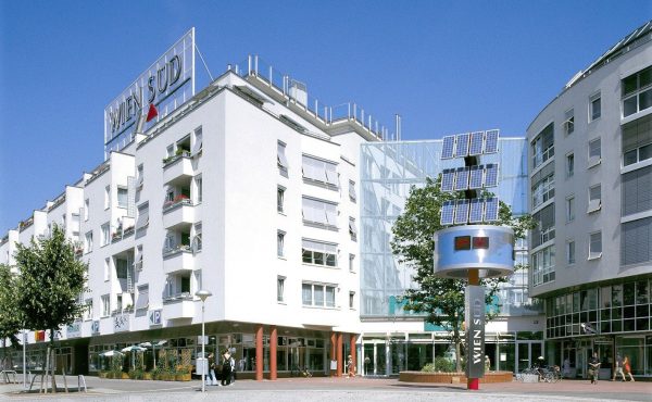 Moderne Wohngebäude mit Solarpanelen und Passanten bei Sonnenschein.