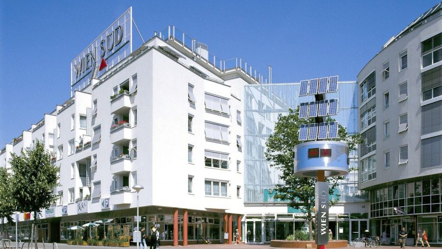 Moderne Wohngebäude mit Solarpanelen und Passanten bei Sonnenschein.