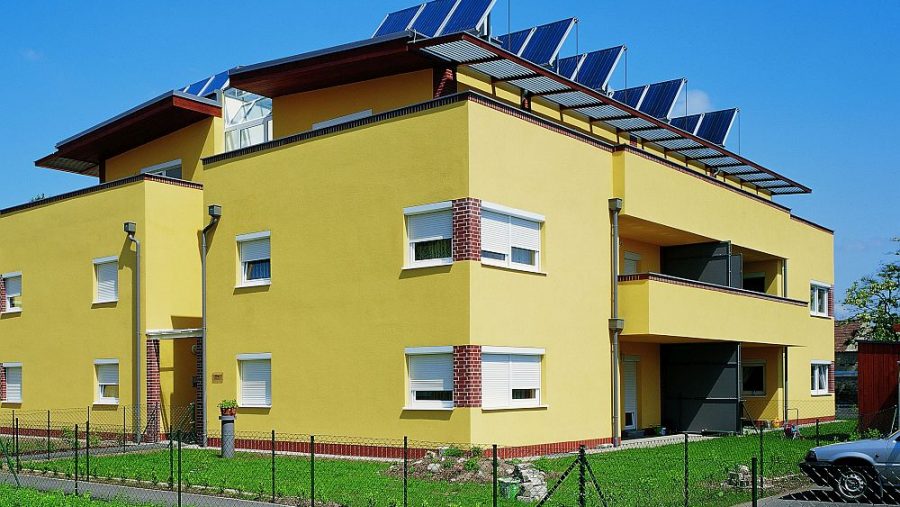 Gelbes Haus mit Solaranlagen auf dem Dach, umgeben von grünem Rasen, an einem sonnigen Tag.