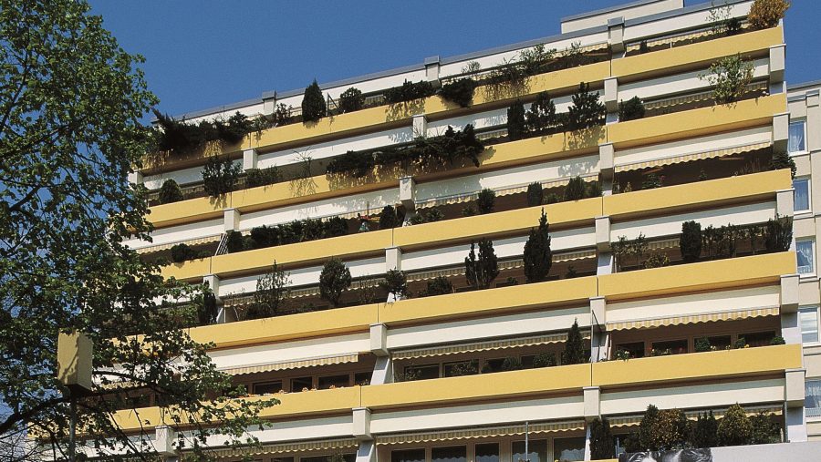 Gelbes Wohngebäude mit Pflanzen auf Balkonen an einem sonnigen Tag.