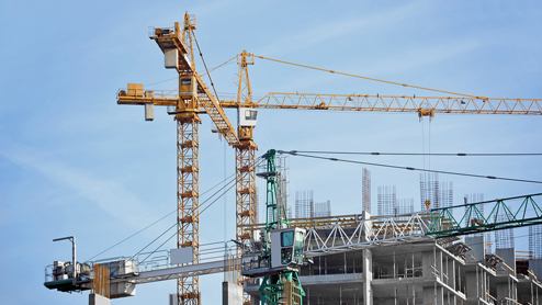 Baustelle mit Kränen und unvollendetem Gebäude unter blauem Himmel.